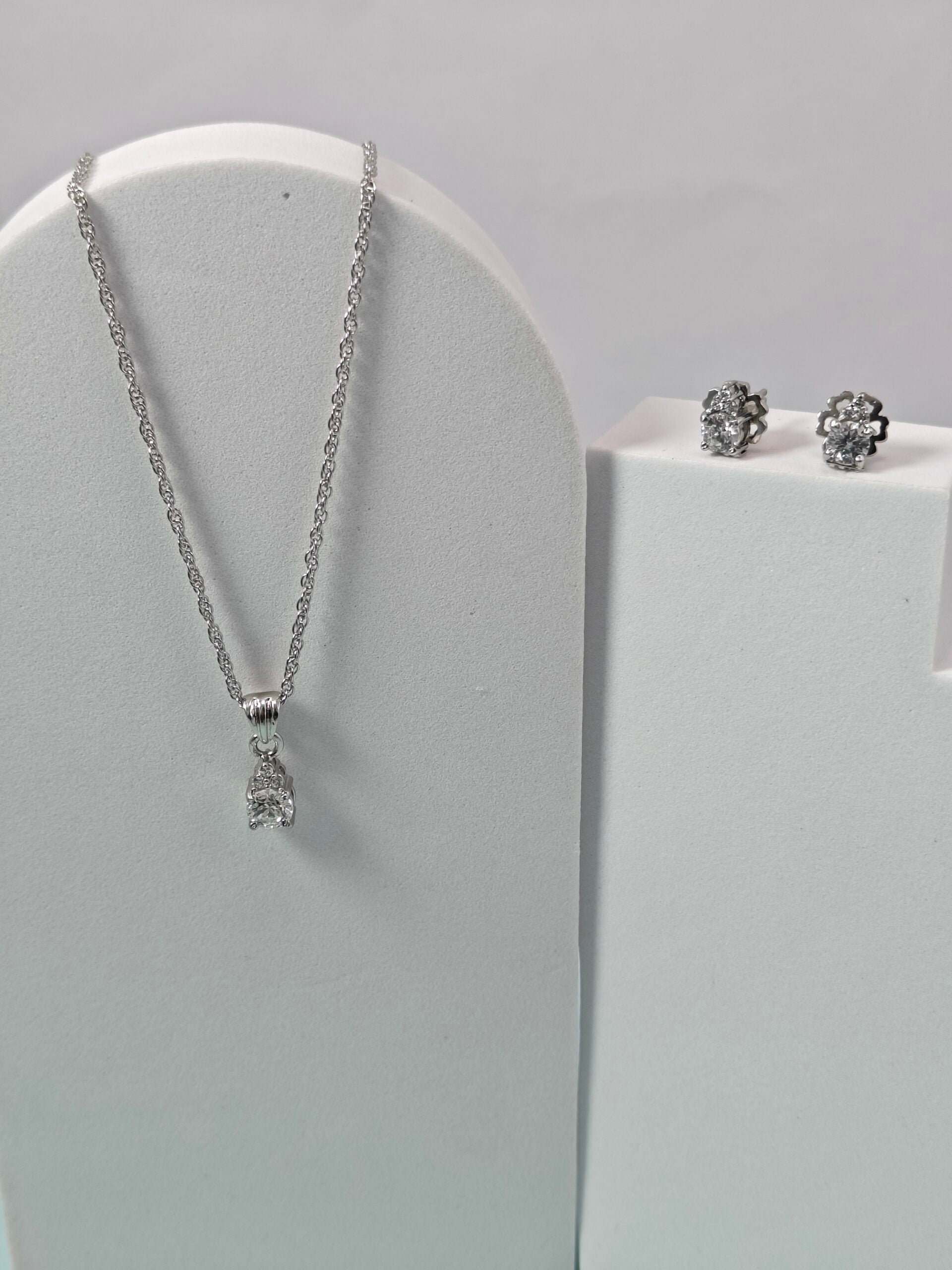 Silver necklace and earrings on a gray stand